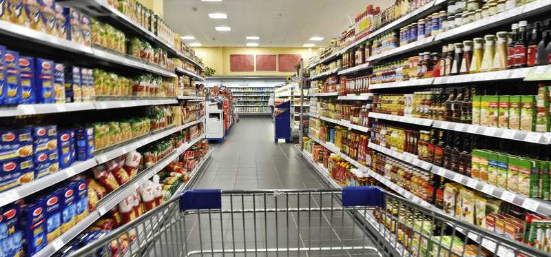 A shopping cart being pushed down a grocery store aisle.