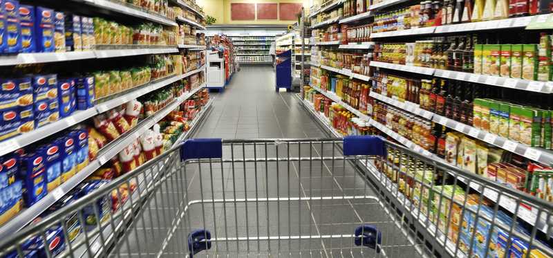 A shopping cart being pushed down a grocery store aisle.