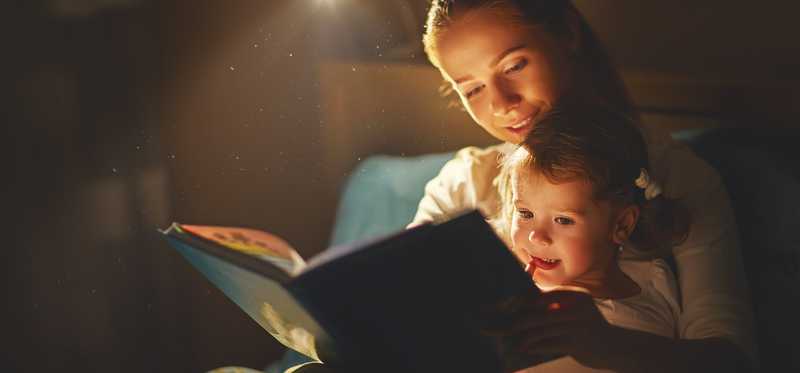 A mother reads her toddle a book by lamplight.r