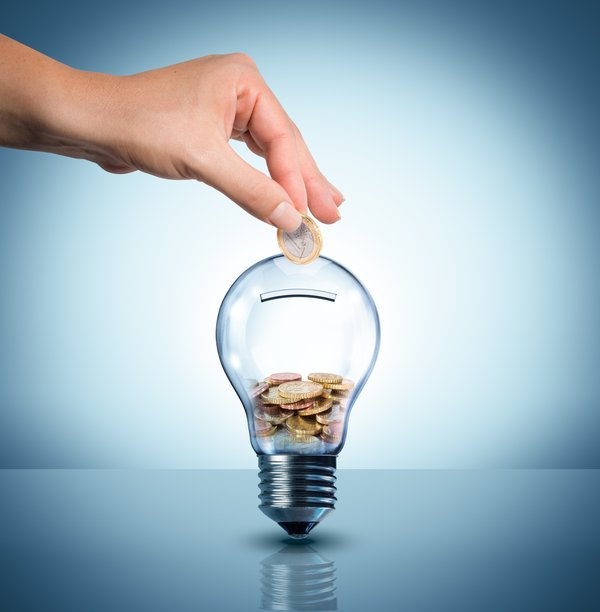 A hand puts coins into a clear bank shaped like a lightbulb.