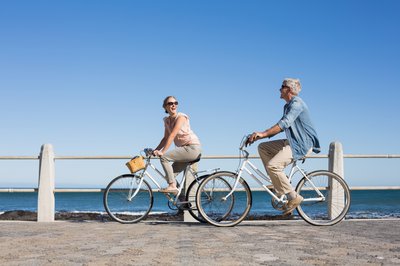 A couple riding bikes on a boardwalk by the beach.