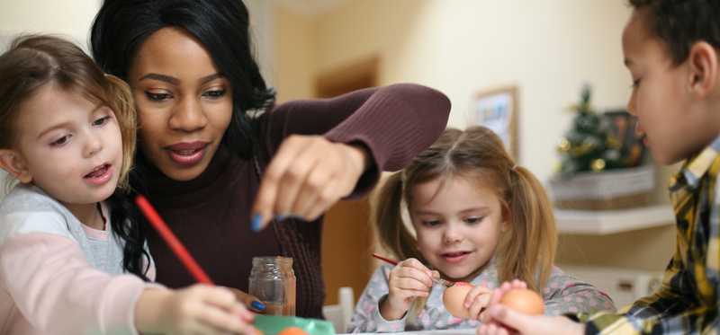 Adult helps three children with crafts.