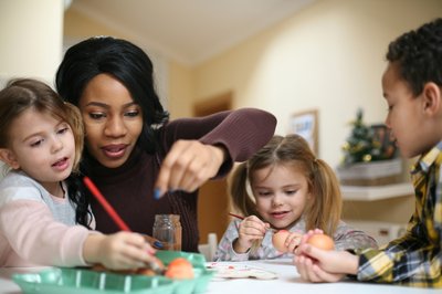 Adult helps three children with crafts.