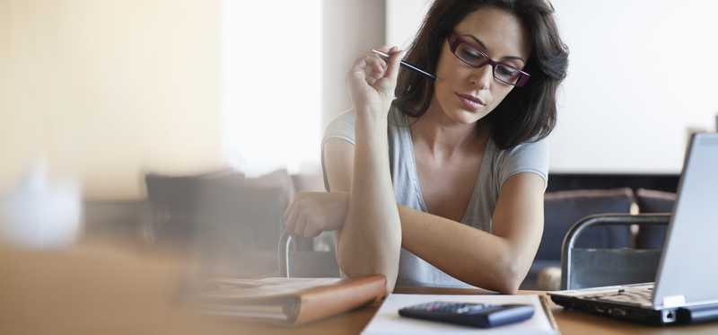 A woman wearing glasses sits over notebook with pen and calculator.