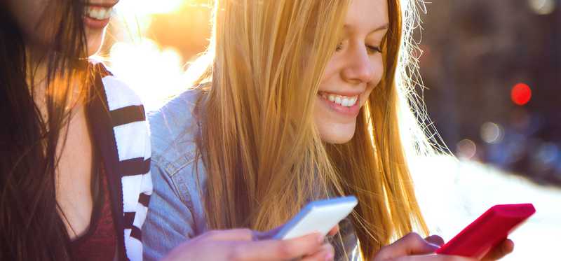 Two young girls use their cell phones.