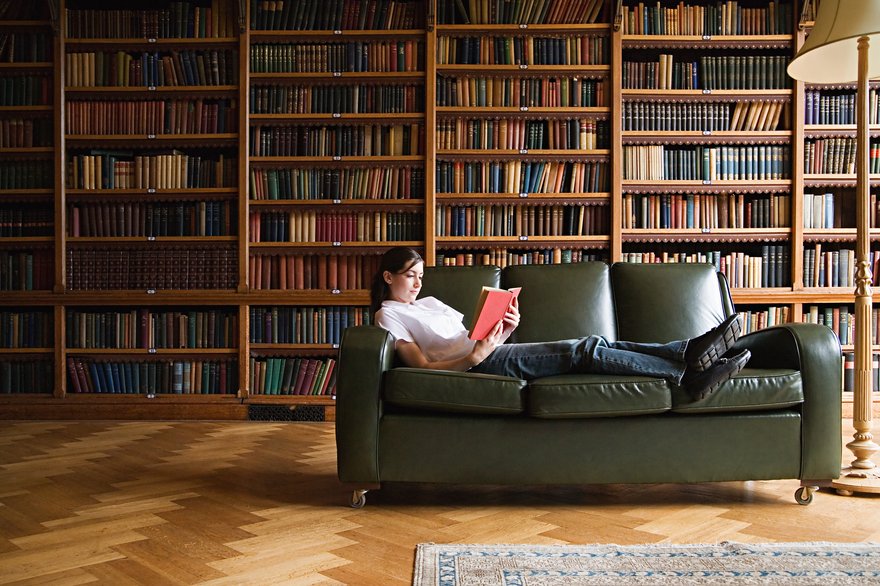 Person reading a book while lying on a couch in a library.
