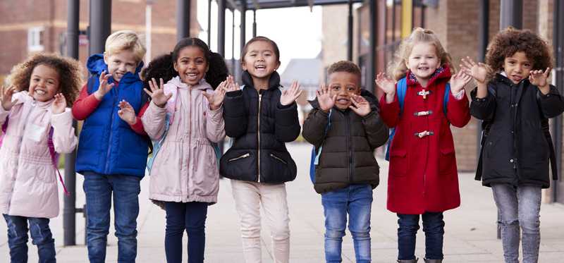 Children outside building are smiling and waving.