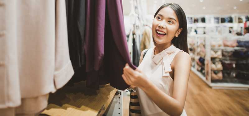 A young woman looking at tops on a clothing rack.