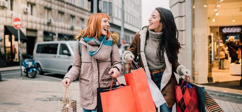 Two people carrying several shopping bags and walking on a city street.