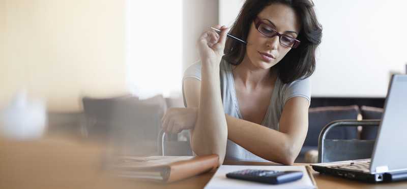 Woman using her laptop with pen in hand and calculator nearby