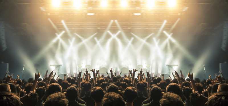 A crowd with hands in the air backlit by stage lights at a concert.