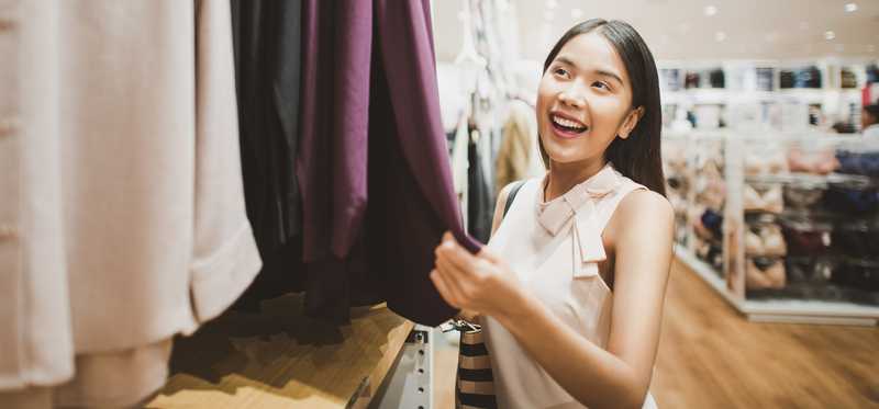 Woman looking at a shirt from a rack of clothing.