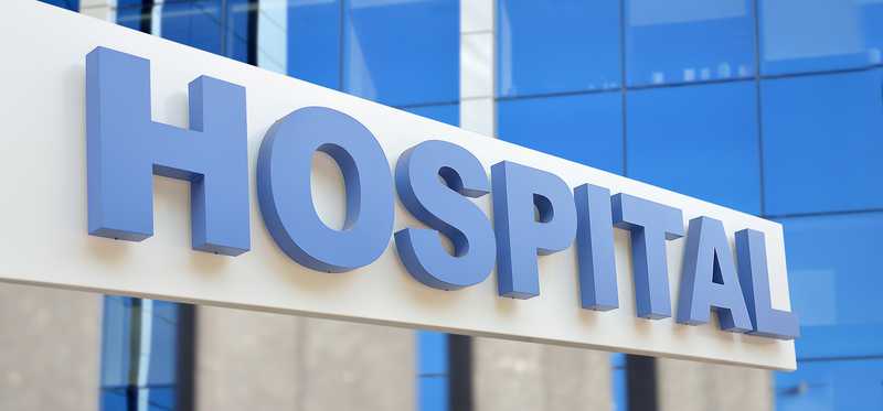 A large white sign that says Hospital in blue letters, with a glass building rising in the background.