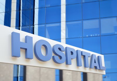 A large white sign that says Hospital in blue letters, with a glass building rising in the background.