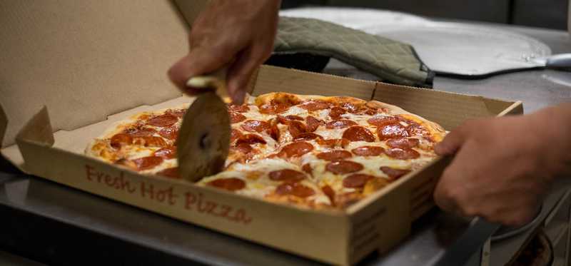 Someone cutting a pizza inside a pizza box.