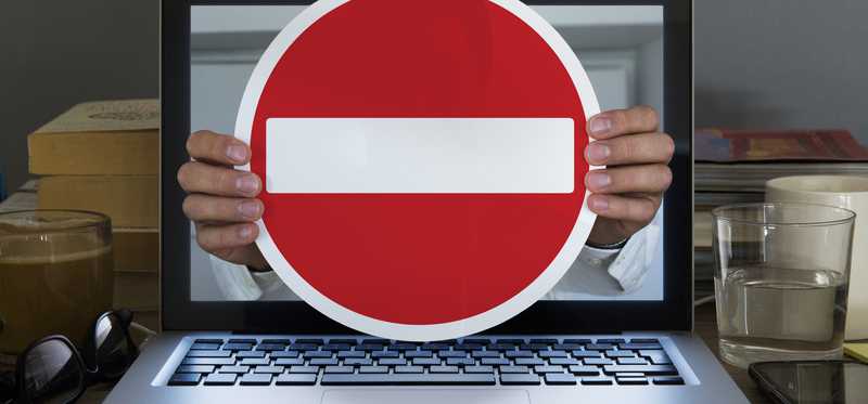 Hand holding Do Not Enter sign coming out of laptop screen