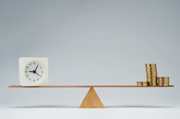 A scale with a clock, representing time, on one side, and a pile of coins, or money, on the other.