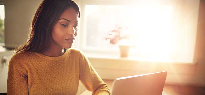 A person uses a laptop in front of a sunny window.