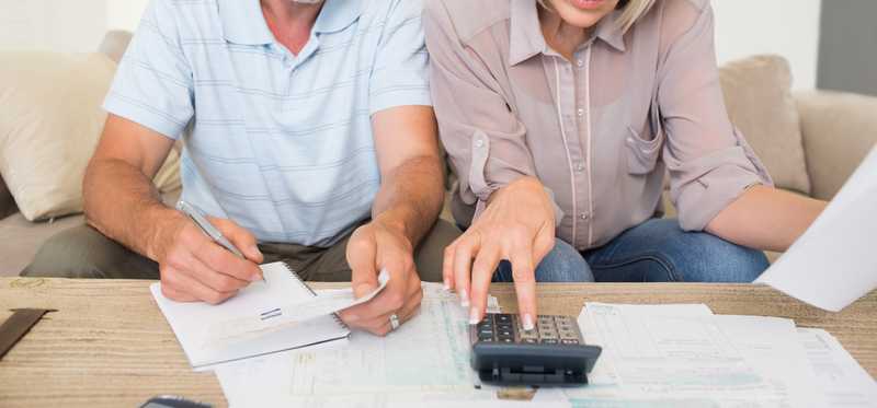 A middle aged couple looking at paperwork and using a calculator.