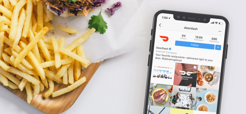 Phone with DoorDash app open sitting next to meal of fries and sandwich.