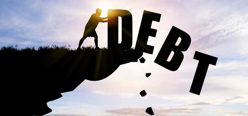 Silhouette of someone pushing giant letters spelling the word Debt off a cliff.