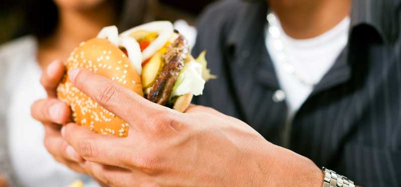 Man holding a burger preparing to take a bite.