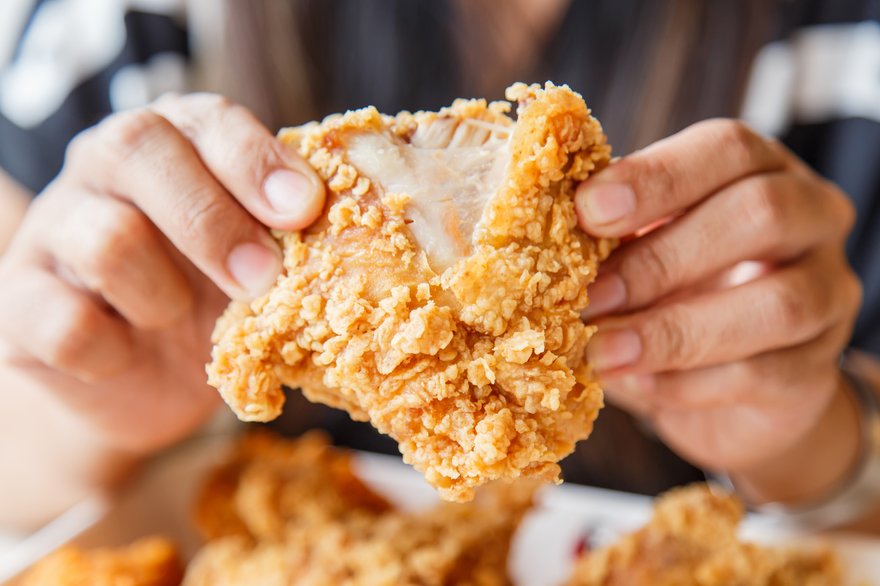 Hands pulling apart a piece of fried chicken.