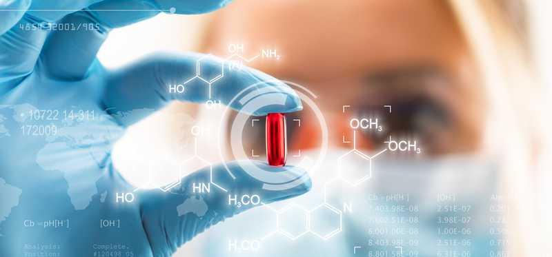 Woman using gloves to hold up and inspect a red pill.