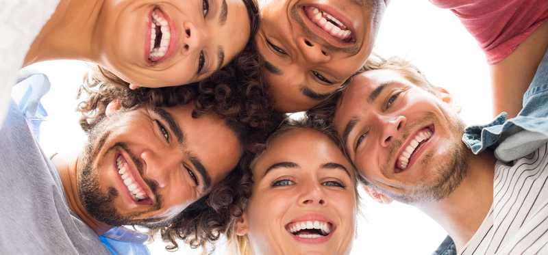 Five heads all leaning together smiling down at a camera.
