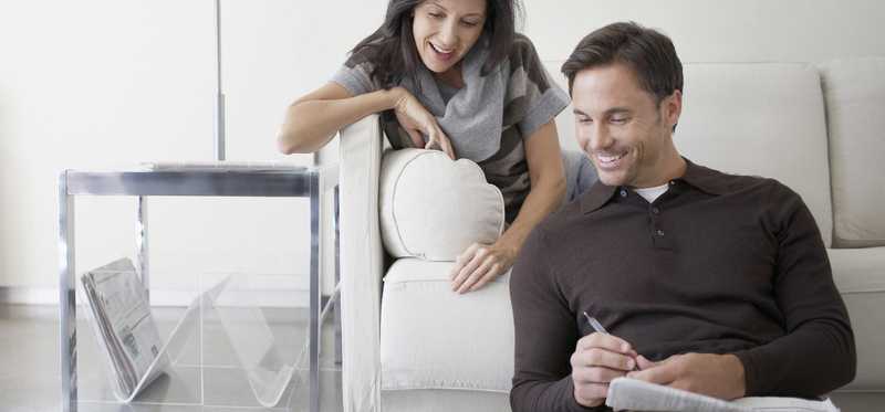 Smiling people sitting in living room while looking at laptop.