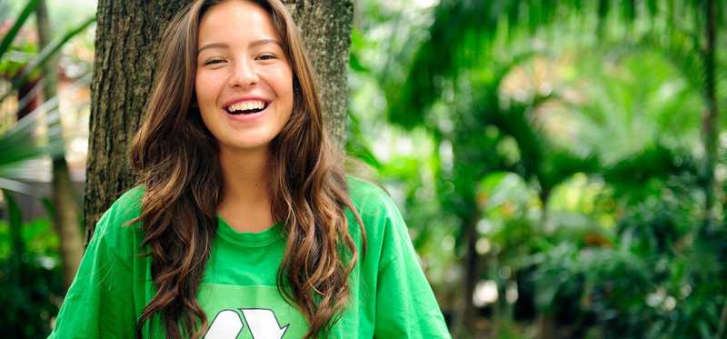 Smiling person standing in front of tree while wearing a green shirt.