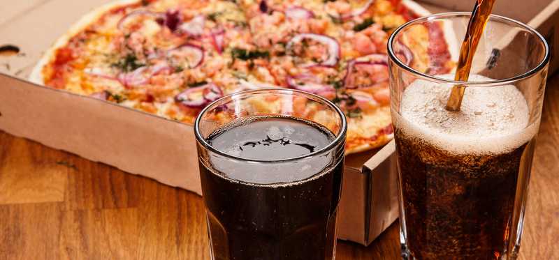 Pouring soda into glasses on table next to pizza
