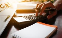 Person's hand typing on a calculator while holding a gold pen.