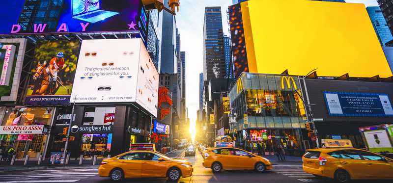 Taxis driving through New York City's Times Square at sunset.