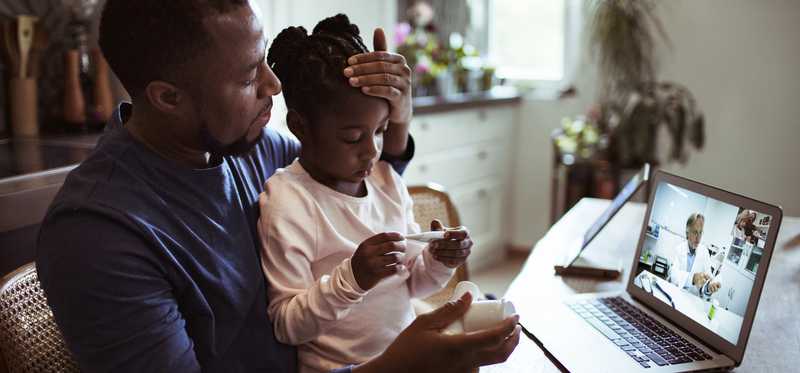 Adult checking a child's temperature during a telehealth doctors appointment.