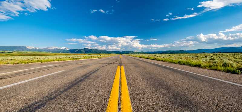 An open highway road with blue skies and greenery on either side