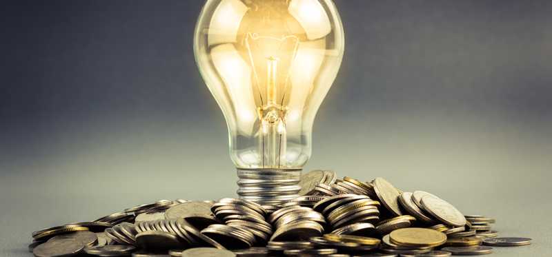 A lit lightbulb with its bottom sitting in a pile of coins.