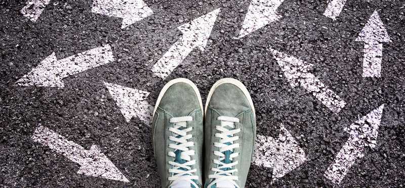 Sneakers standing on pavement that is covered in various arrows pointing different directions.