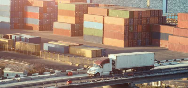 Truck drives past docks with cargo containers.