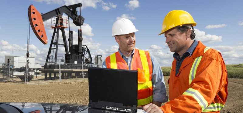 Two people talking with an oil derrick in the near background.