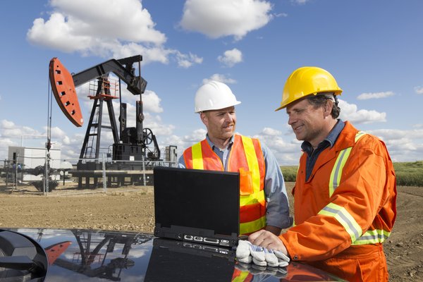 Two people talking with an oil derrick in the near background.