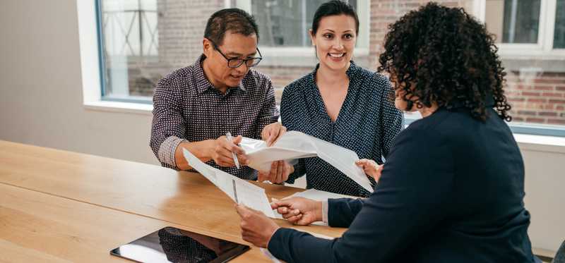 Three people sitting at table reviewing documents.