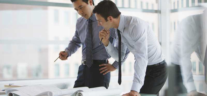 Two professional men standing over a table reviewing documents.