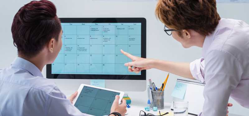 Two professionals looking at a calendar on a computer screen.