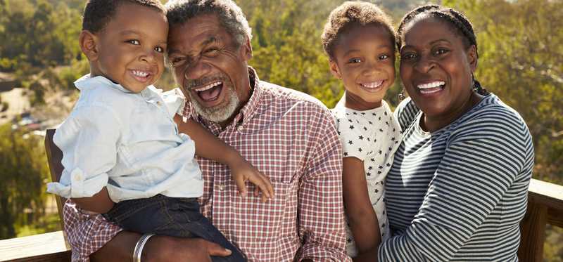 two senior adults standing on outdoor observation deck on a sunny day holding small children and smiling