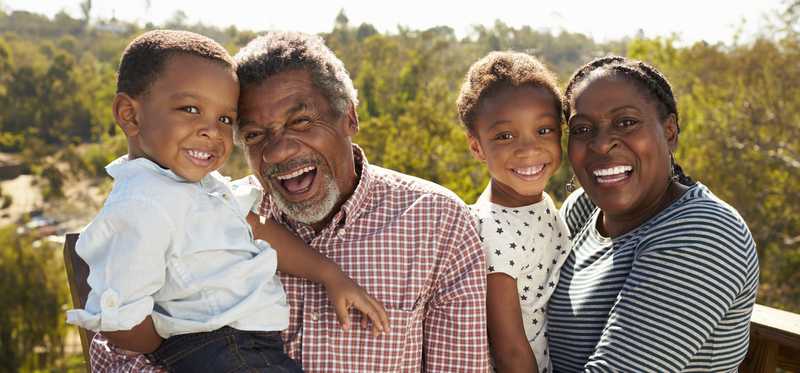 Two adults standing on outdoor observation deck on a sunny day while holding small children and smiling.
