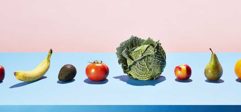 Vegan foods, all types of fruits and vegetables lined up on a blue table.