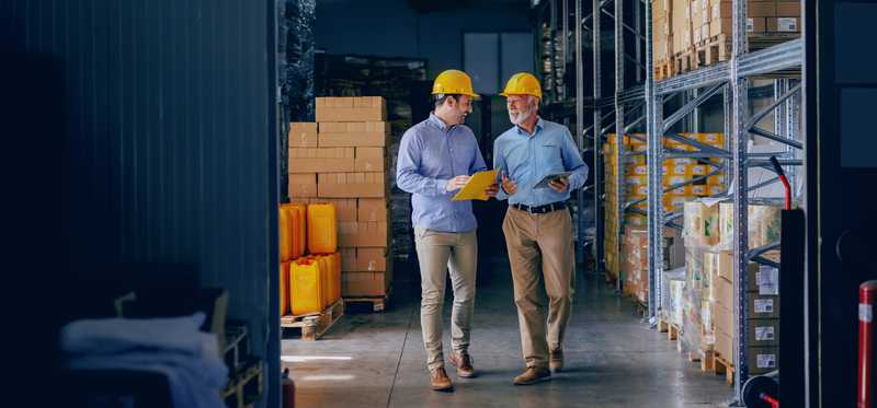 Two warehouse workers wearing hard hats in warehouse aisle
