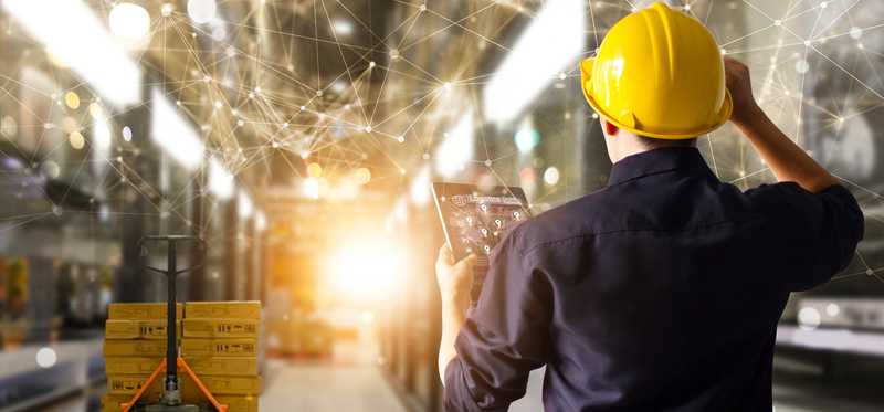 A person in a warehouse holding a tablet with superimposed graphics displaying connective technology in use.