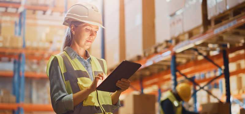 Person standing in warehouse and holding a tablet.
